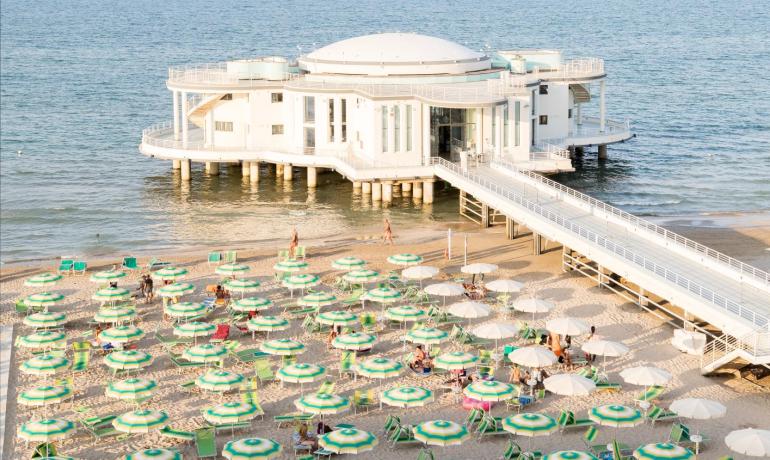 Spiaggia soleggiata con ombrelloni colorati e edificio sul mare.